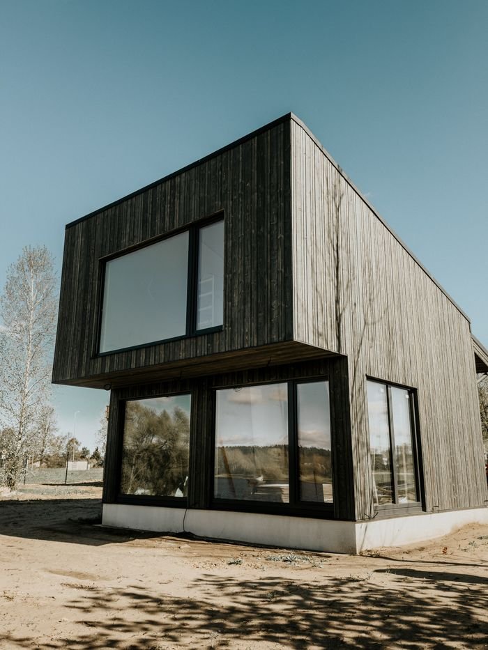 Modern wooden house with large windows, located outdoors with clear skies.