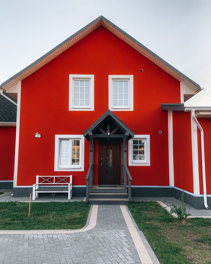 A modern red house with white trim, front porch, and neatly paved path, offering a warm and welcoming feel.